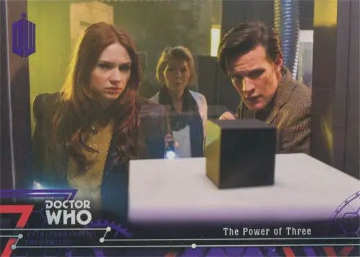 Three people examining a purple parallel chase card near a black cube on a table