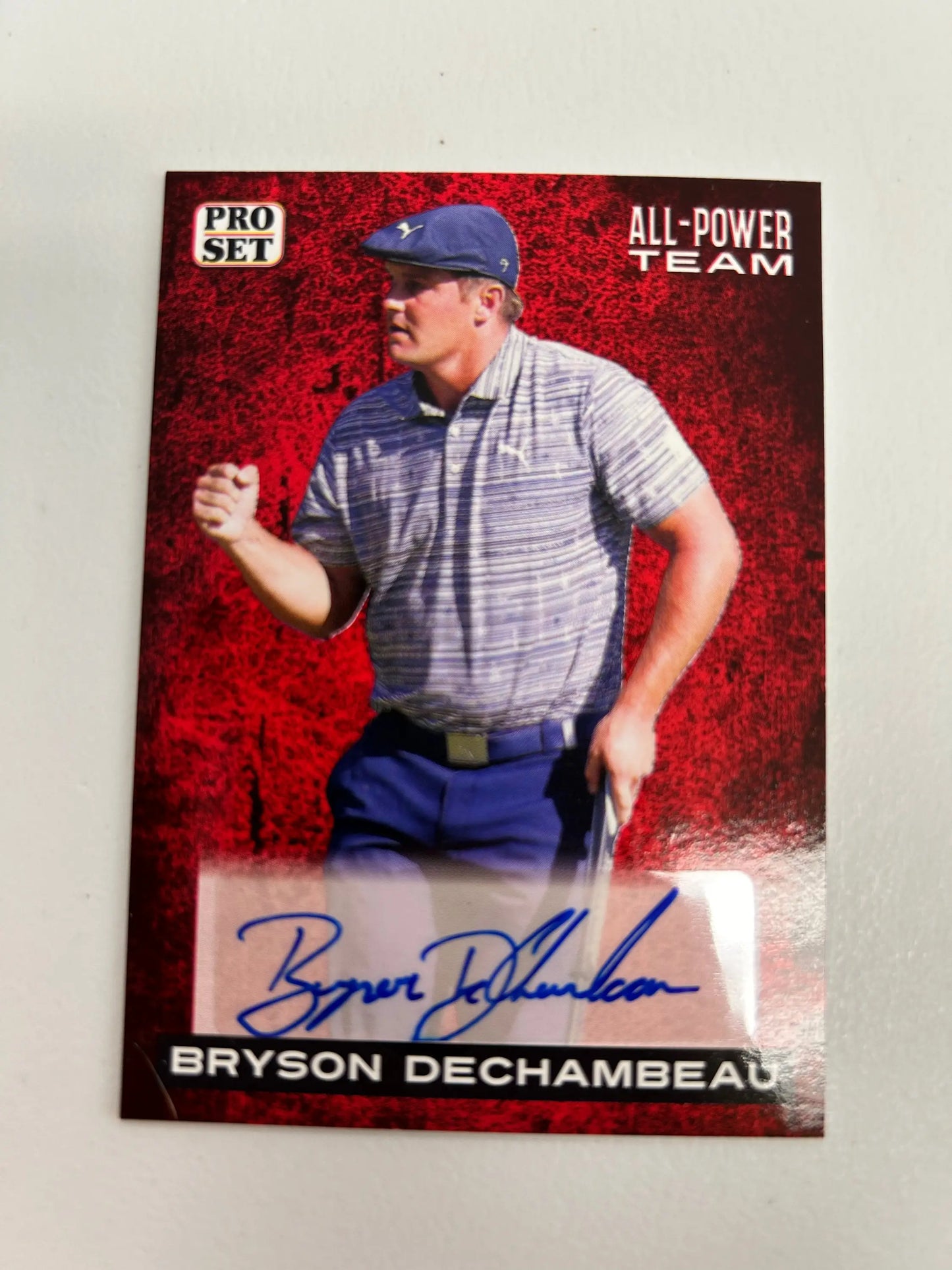 Signed Bryson Dechambeau trading card in blue cap, striped shirt, red background