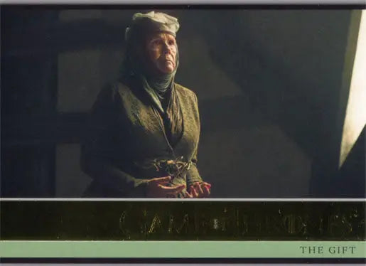 Elderly person in headscarf and olive clothing holding gold parallel trading card