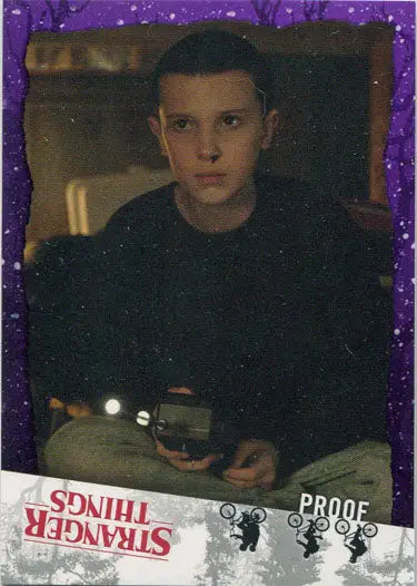 Young person in dark shirt holding an electronic device near Stranger Things purple parallel card