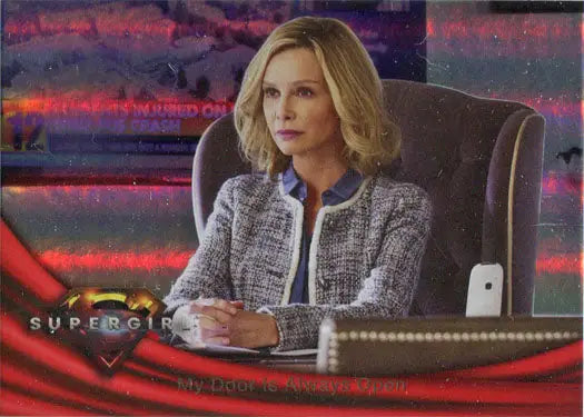 Woman with blonde hair in tweed jacket at desk beside Supergirl Season 1 Rainbow Foil Board