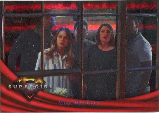 Four people visible through window panes illuminated by red light in Supergirl foil card