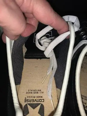 Person adjusting white laces on Tony Dorsett Converse football shoes with Dallas Cowboys theme